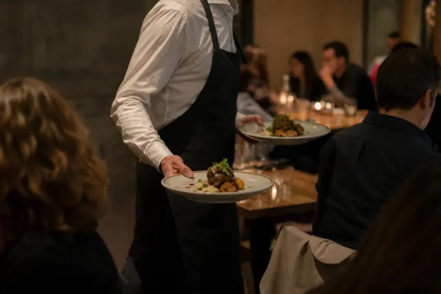 Serveur portant des assiettes dans une salle de restaurant le soir